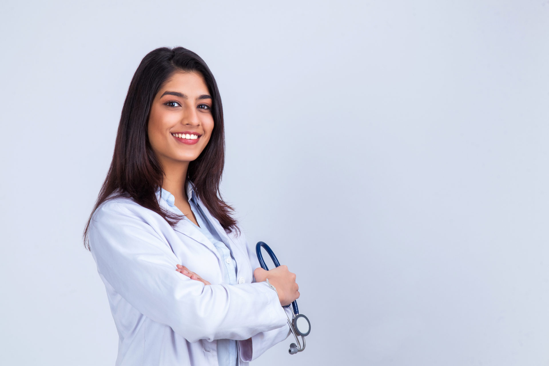 Indian female doctor in white coat with stethoscope, waist up.
