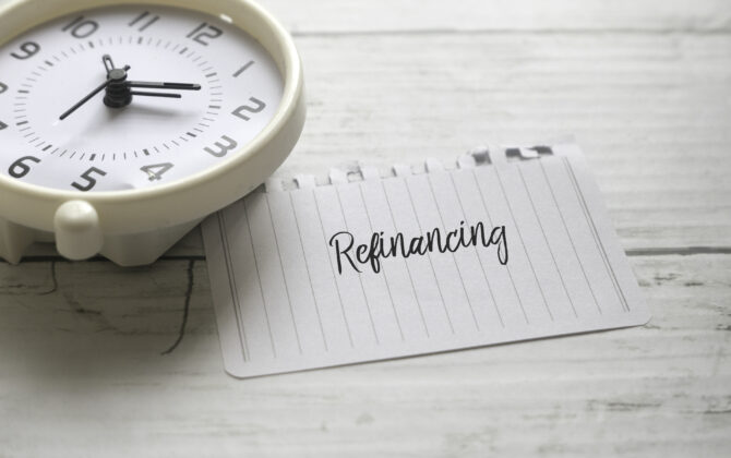Selective focus of table clock and paper written with Refinancing on white wooden background.